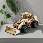 An assembled 3D wooden mechanical wheel loader displayed as a sophisticated home decor piece on a grey stone surface with shadows of green leaves.