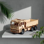 A completed Dilruo 3D wooden dump truck model displayed as a sophisticated home decor piece on a minimalist shelf with green plants.